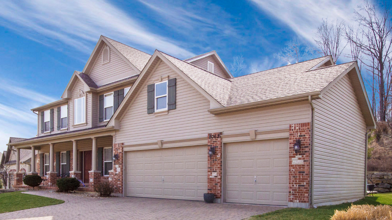 A multifamily home with brown brick, two car garage and tan roof shingles